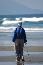 Elderly man walking on beach with the aid of a standard cane